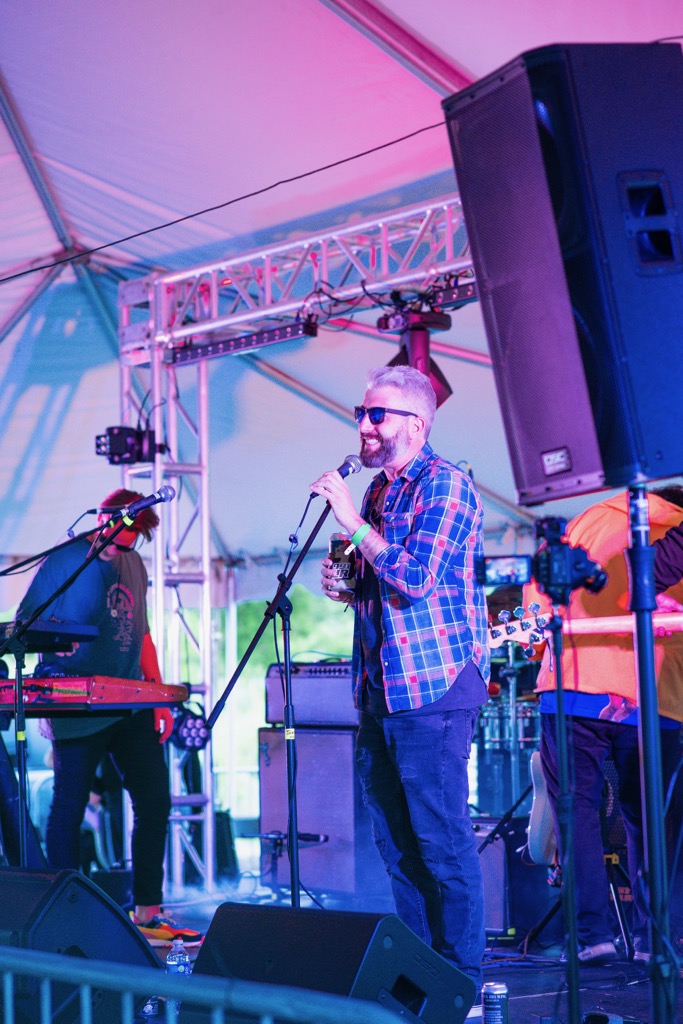 Jon Kamal on stage at an outdoor festival, smiling at the mic with the band behind him