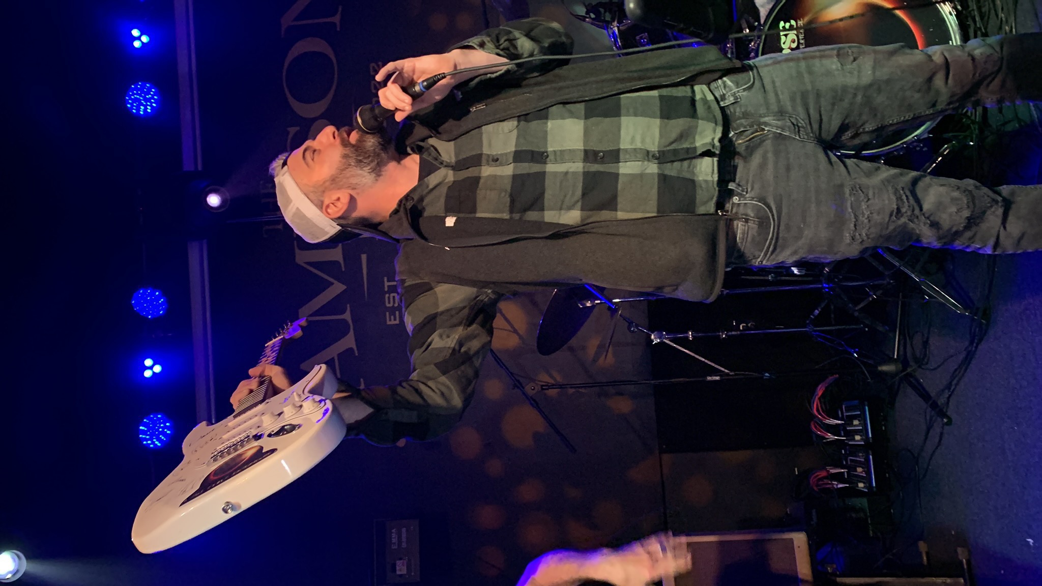 Jon Kamal on stage holding a guitar overhead while MCing a live show